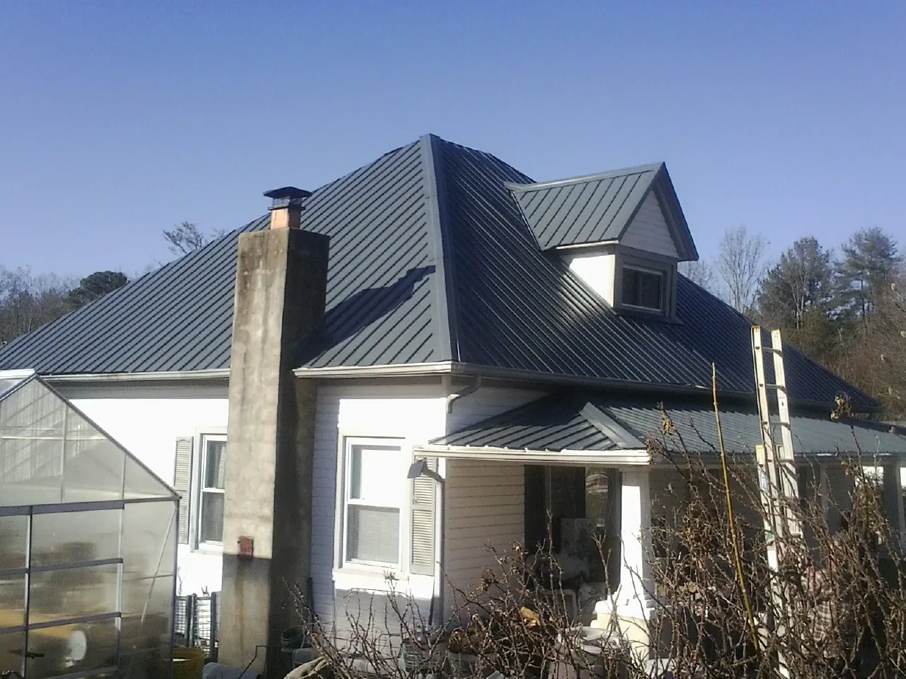 Dark blue standing seam metal roof on a white farmhouse with dormer — Slate & Tile Roof Repair by Roofing Brothers in Okmulgee
