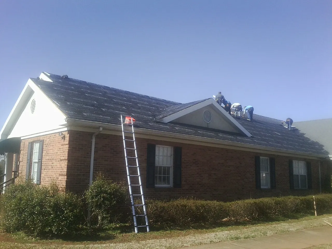 Crew tearing shingles off a brick ranch roof with a ladder set — Emergency Roof Repair work by our crew in Okmulgee