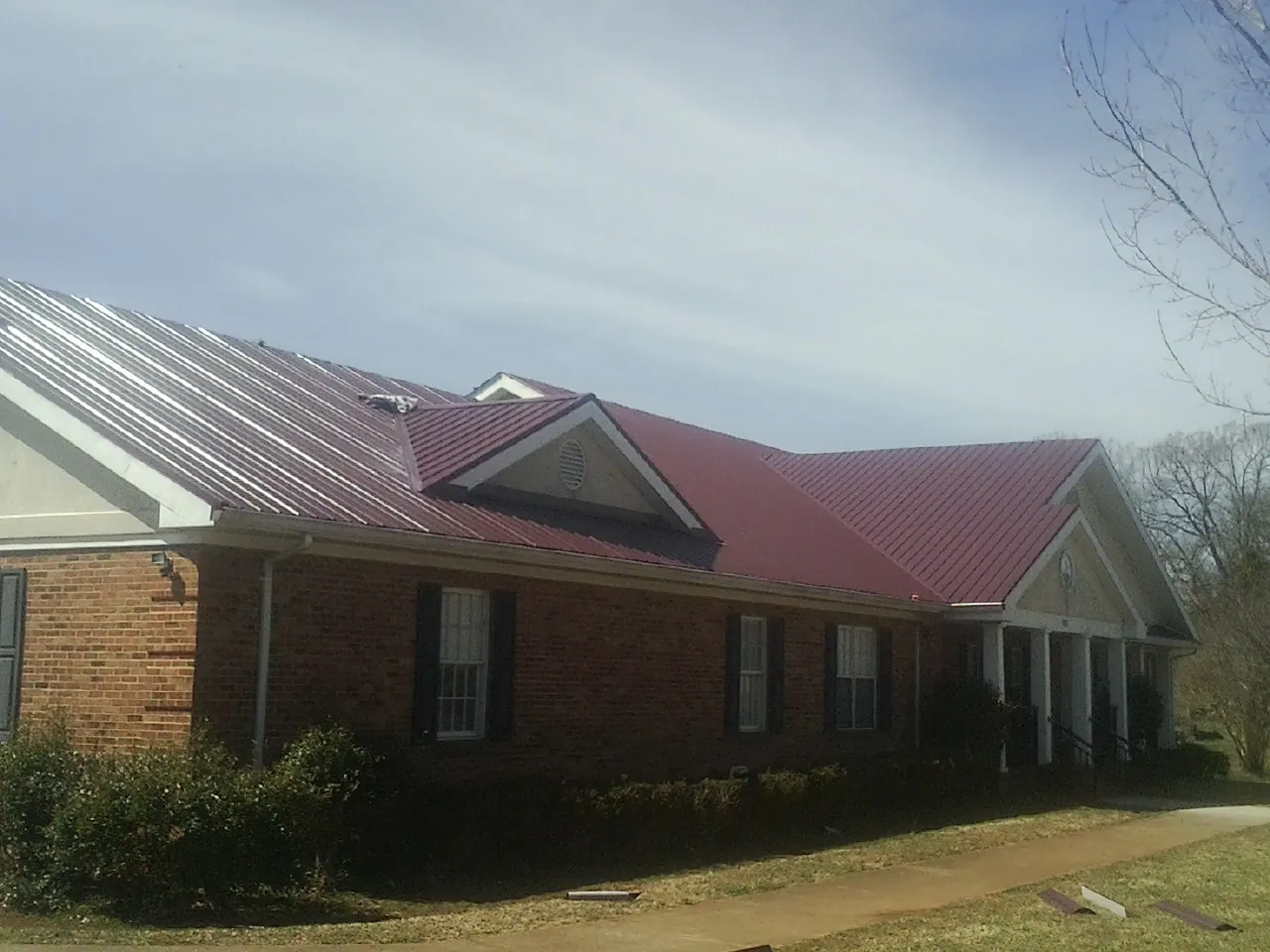 Red metal roof with gabled entries on a long brick building, from a Hail Damage Roof Repair job in Okmulgee