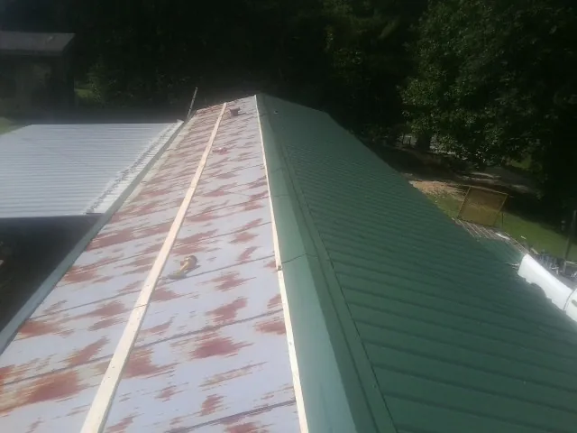 Old rusted panels beside newly installed green metal roofing — Wind Damage Roof Repair by Roofing Brothers in Okmulgee