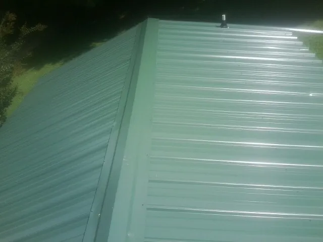 New green metal panels meeting at the ridge of a roof — Flat Roof Repair work by our crew in Okmulgee