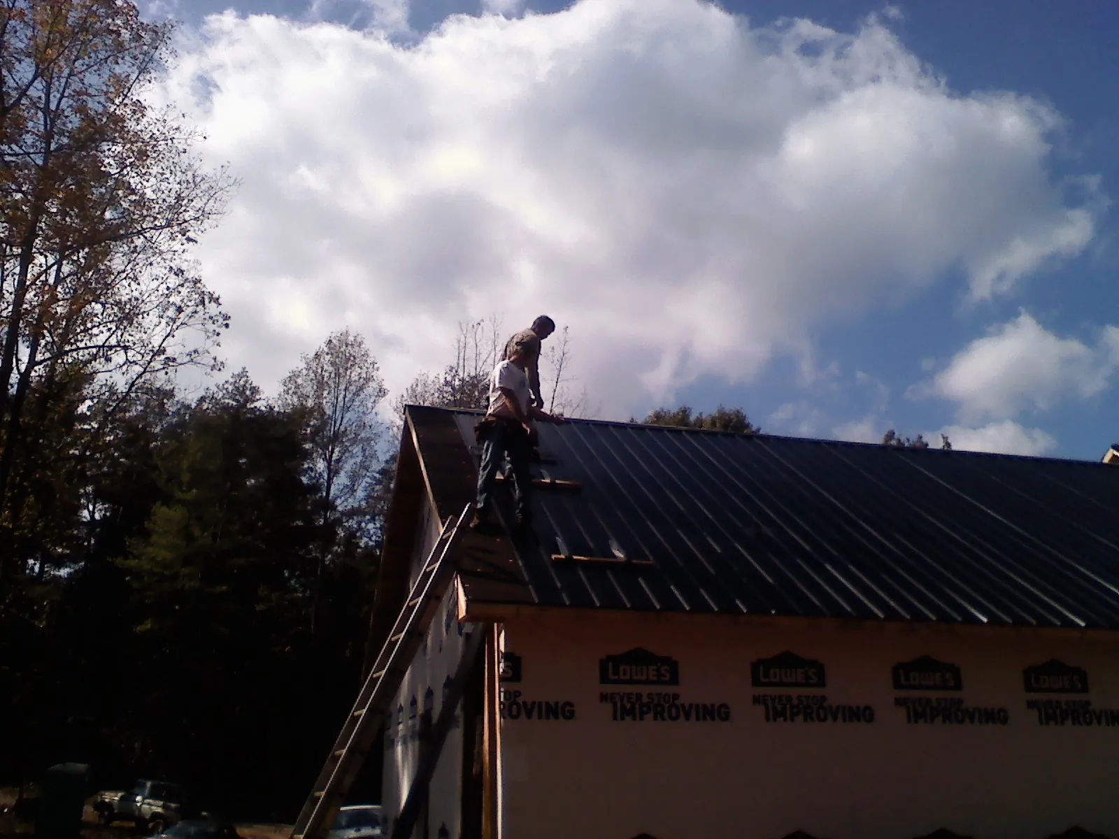 Roofer fastening dark metal panels high against a cloudy sky, from a Roof Inspection job in Okmulgee