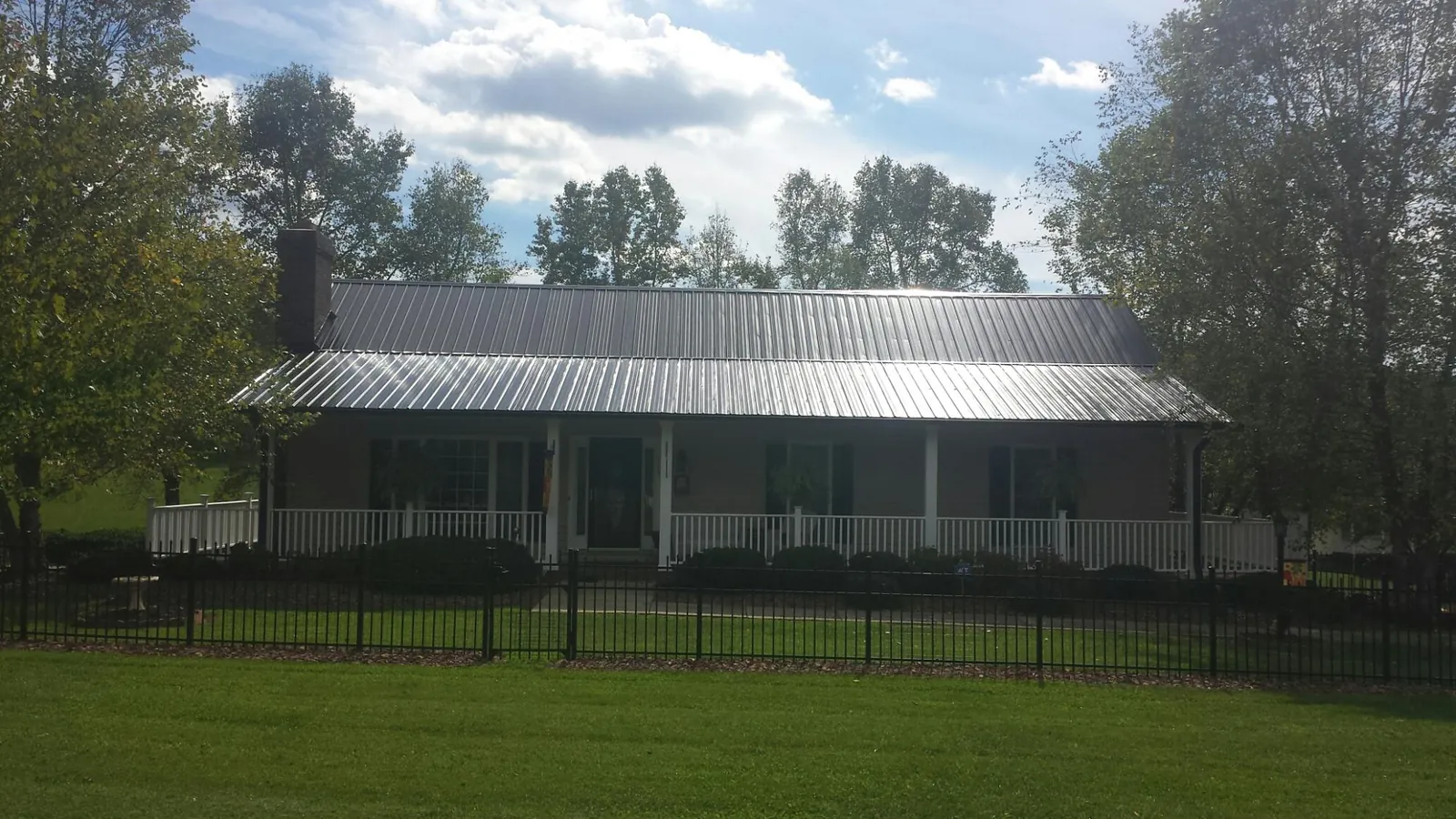 Gray metal roof on a brick ranch with a full width front porch — Gutter Guard Installation work by our crew in Okmulgee