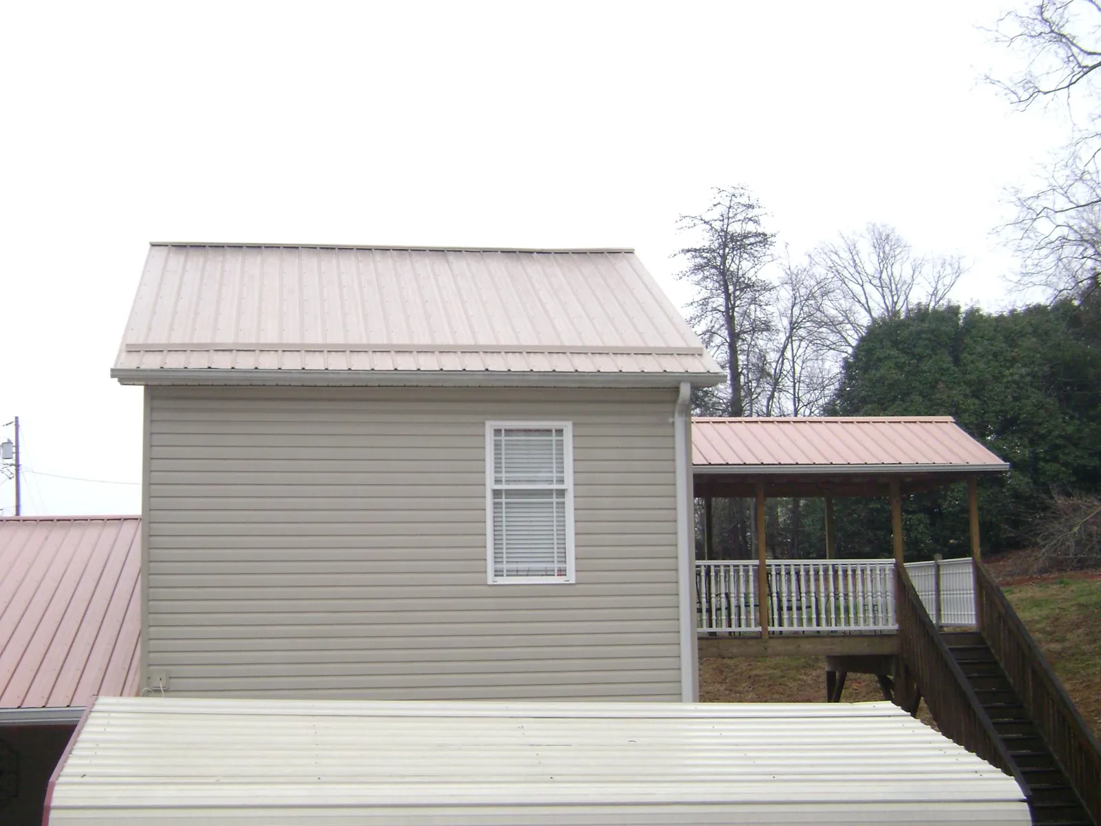 Tan metal roofs on a two story addition and attached porch, from a Roof Replacement job in Okmulgee