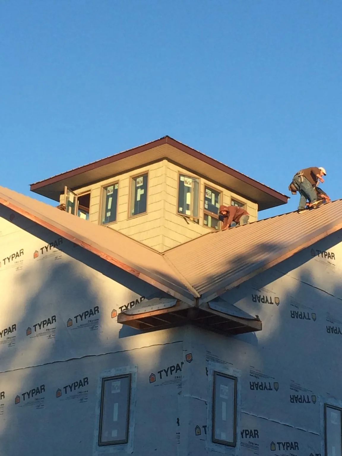 Roofers working around a rooftop cupola on a new metal roof at sunset — Roof Waterproofing in Okmulgee by Roofing Brothers